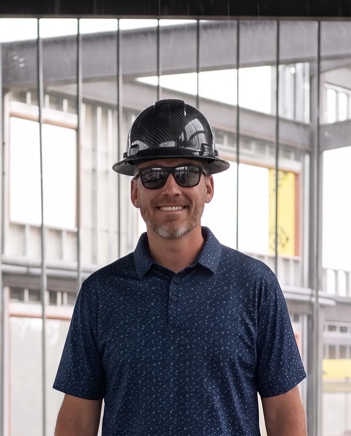 Josh, founder of Kalin Group, in a black carbon-fiber hard hat inside a steel-framed building under construction