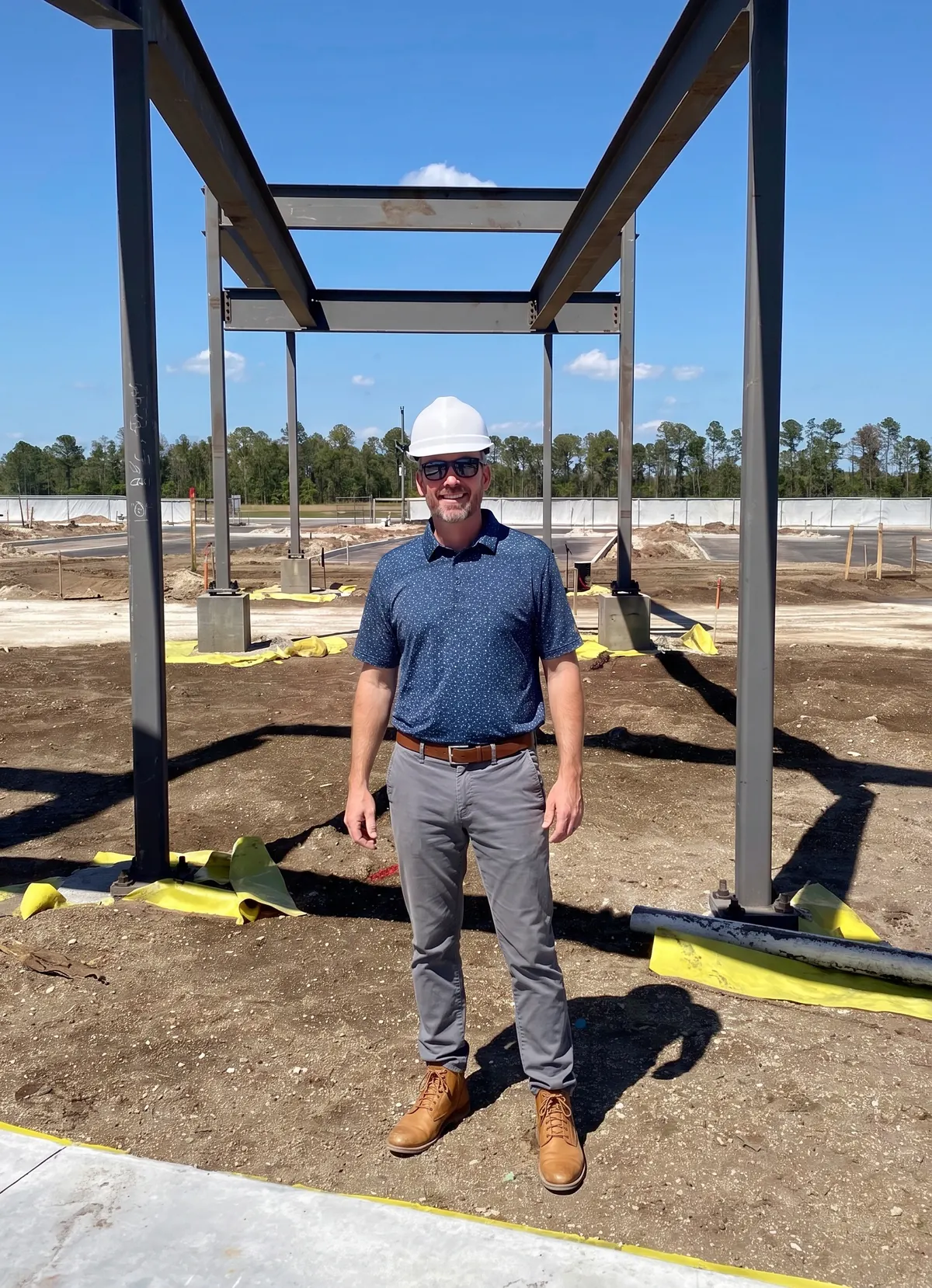 Josh in a white hard hat on a job site, standing under a new steel frame